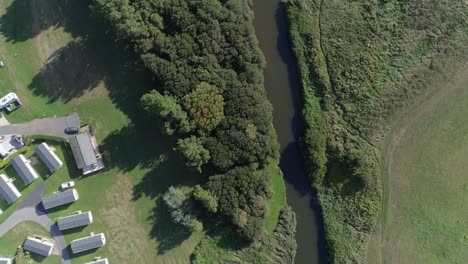 Top-down-aerial-of-a-river-and-the-edge-of-a-holiday-caravan-park