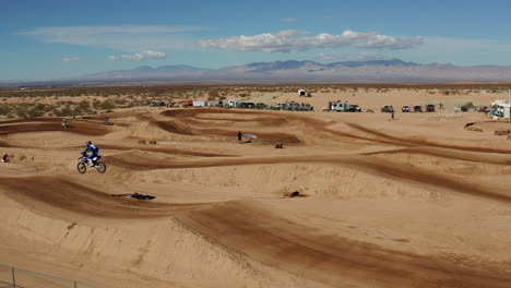 Motorcycle-rider-jumping-off-ramp-on-dirt-track-in-Mojave-Desert,-Aerial-Slowmo
