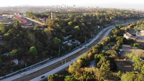 Aerial-view-of-winding-highway-cutting-through-trees-and-a-small-village