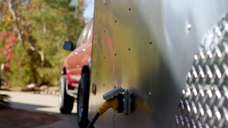 Vertical-slide-down-shot-along-the-side-of-a-metal-teardrop-travel-trailer-and-suv-towing-vehicle-with-an-electrical-hook-up-plug-at-a-camp-site