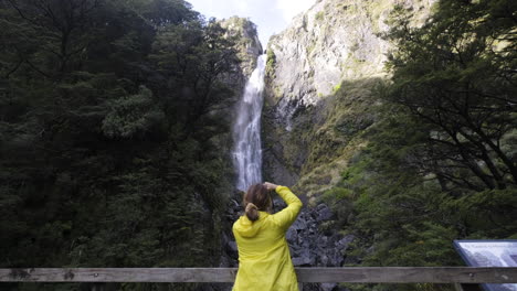 Chica-Con-Chaqueta-Amarilla-Fotografiando-Una-Gran-Cascada-En-Nueva-Zelanda