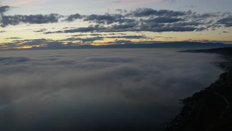 Aerial-panning-over-fog-covering-lake-Léman-at-sunset
