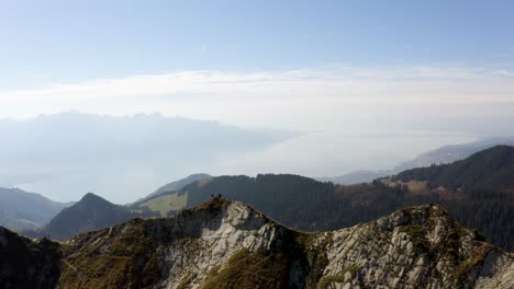 Short-aerial-orbit-with-hikers-standing-out-as-shadow-on-summit-"La-Cape-au-Moine"-with-Lake-Léman-in-the-background,-Vaud---Switzerland