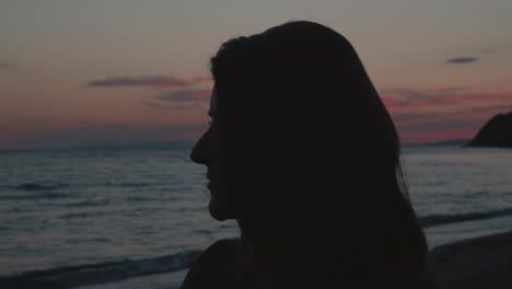 Eine-Nahaufnahme-Eines-Mädchens,-Das-Bei-Sonnenuntergang-Am-Strand-Steht-Und-Auf-Das-Meer-Blickt