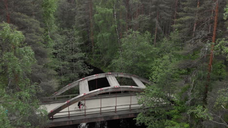 Drone-flight-over-a-bridge-in-the-middle-of-a-dense-forest-and-a-person-traveling-by-bicycle