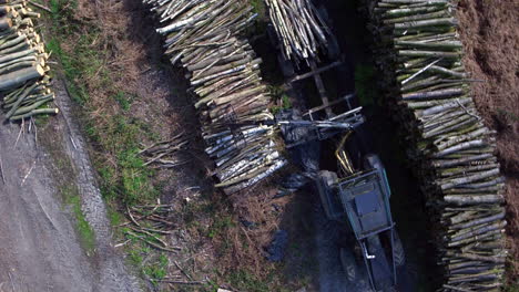 Top-down-aerial-view-of-a-tractor-loading-lengths-of-wood-onto-a-trailer-in-a-woodyard