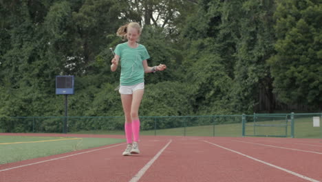 Cute-young-girl-teenager-walks-on-track-twirling-her-headphones-in-slow-motion