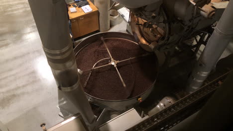 top-shot-of-a-spinning-coffee-roasting-wheel-in-a-roasting-company-with-a-man-working-in-the-background