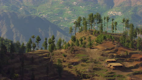 Trees-at-top-of-the-mountain-aerial-flight,-showing-a-small-hut-at-the-mountain,-Majestic-and-beautiful-mountains-with-houses-at-the-background