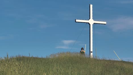 A-woman-walks-toward-a-large-white-cross-on-top-of-a-hill