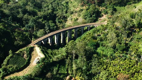 Aerial-of-famous-nine-arch-bridge-in-Ella,-Sri-Lanka-with-blue-train