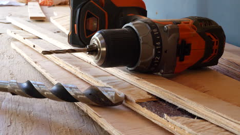 A-power-tool-drill-on-a-stack-of-plywood-lumber-boards-with-a-drill-bit-on-a-construction-site