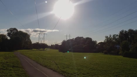 Wide-shot-of-a-trail-with-bikers-and-walkers-on-a-summer-day-with-huge-power-lines-overhead-and-the-sun-in-the-distance