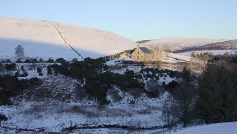 Luftaufnahme-Einer-Von-Schnee-Umgebenen-Kirche-Bei-Sonnenuntergang-In-Der-Nähe-Von-Laggan,-Moray,-Schottland---Vorwärtsschuss