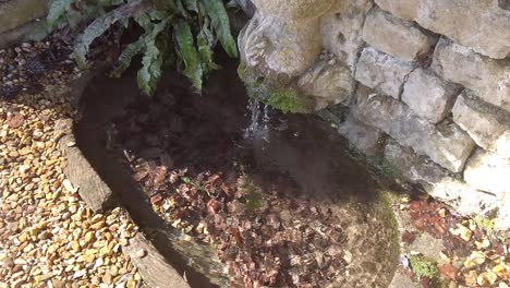 Wasser,-Das-Aus-Einer-Alten-Steinmauer-In-Einen-Kleinen-Teich-Fließt