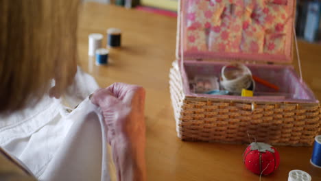 An-old-woman-sewing-a-new-button-onto-a-white-shirt-by-hand-to-repair-it-with-her-needle-and-thread