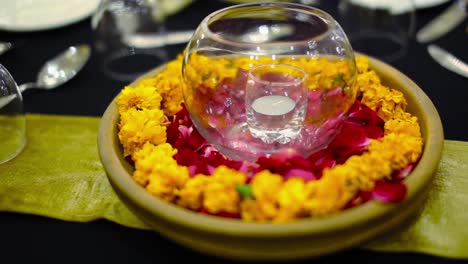 Marry-gold-flowers-and-rose-petals-set-in-the-plate-with-candle-in-the-glass-at-the-dinning-table