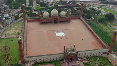 Lahore,-Pakistán,-Rotación-Aérea-Superior-Y-Vista-De-Alejamiento-De-La-Mezquita-Badshahi,-Rodeada-De-Parques,-Visitantes-Damas,-Caballeros-Y-Niños-Están-En-La-Mezquita,-Adoradores-En-El-Suelo-De-La-Mezquita