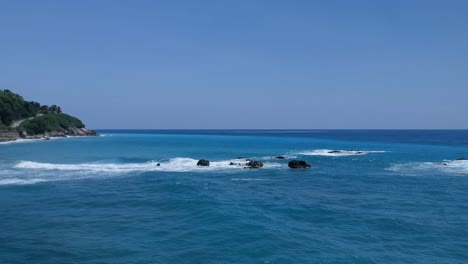 Low-angle,-aerial-view-of-clear-turquoise-Caribbean-water-as-waves-break-over-large-rocks-in-the-surf
