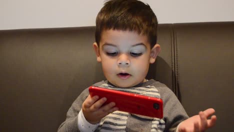 Süßer-Zweijähriger-Junge-Hält-Smartphone-Und-Erklärt-Etwas