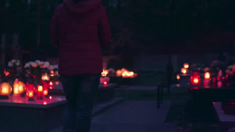 Woman-walking-through-cemetery-at-night,-candles-are-shining-in-the-dark