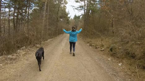 Girl-walking-on-mountain-trail-in-forest-with-black-dog,-during-autumn