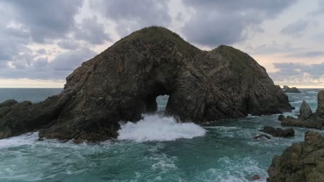 Aerial-cinematic-shot-of-waves-passing-throw-the-cave-of-a-rock-formation-Zipolite,-Oaxaca