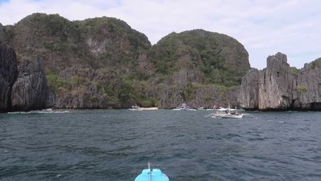 Boat-drifting-on-the-turquoise-water-limestone-cliffs-tropical-Islands-tourist-paradise,-Philippines-Drifting-past-limestone-cliffs,-foliage,-and-white-sand-over-calm,-clear-waters