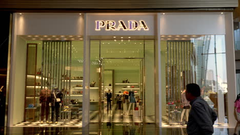Shoppers---tourists-passing-across-front-of-Prada-storefront-in-luxury-shopping-mall,-Icon-Siam,-Bangkok,-Thailand