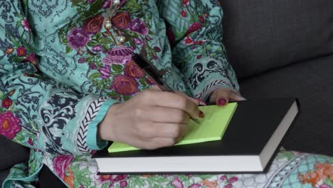 Medium-Close-Up-of-Young-Asian-Indian-female's-hand-in-salwar-kameez-writing-down-notes-with-pen-sitting-down-indoors