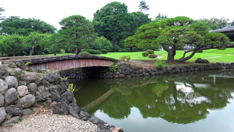 Puente-De-Madera-En-El-Jardín-Tradicional-Japonés-Con-Reflejo-De-árboles-En-El-Lago