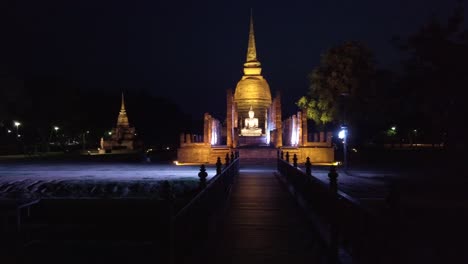 Parque-Histórico-De-Ukhothai-Tailandia-Escultura-De-Buda-Iluminada-Por-La-Noche-Toma-Panorámica-De-Izquierda-A-Derecha