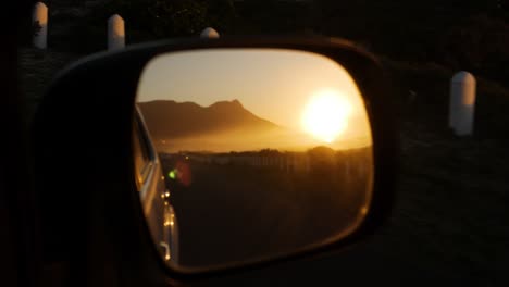 Sunset-next-to-mountain-caught-in-side-mirror-of-driving-car