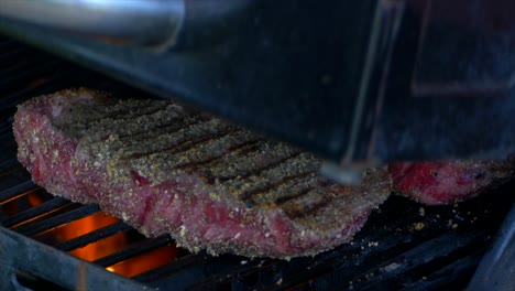 Two-thick-and-juicy-rib-eye-steaks-are-covered-as-a-grills-lid-is-closed-in-slow-motion