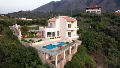 Aerial-Counter-Clockwise-Fly-Around-of-Luxury-Greek-Villa-with-Pool-with-Mountains-in-Background-and-Green-Foliage-in-Foreground---Car-on-Drive