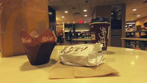 Editorial,-view-of-McDonald's-meal-on-table,-cafe-,-sandwich-and-muffin-on-table-in-the-fast-food-restaurant-with-view-of-clients-passing
