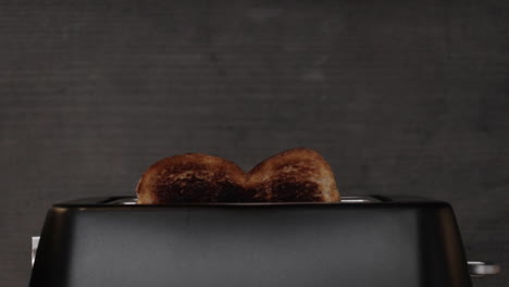 Eine-Zeitlupenaufnahme-Von-Verbranntem-Toast,-Der-Aus-Einem-Mattschwarzen-Toaster-Herausspringt-Und-Aus-Dem-Rauch-Aufsteigt