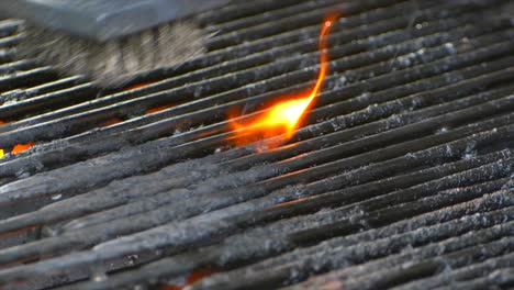 A-wire-brush-cleans-a-grill-as-a-small-flame-burns-on-some-old-food