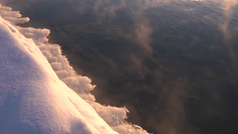 Nahaufnahme-Von-Eis,-Das-Sich-Im-Winter-Auf-Einem-Zugefrorenen-See-Neben-Einem-Schneebedeckten-Ufer-Bildet