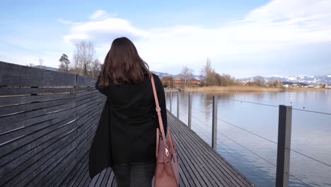 Following-shot-of-a-young-asian-woman-walking-and-looking-back-on-a-pier-with-a-big-smile-in-slow-motion-in-Rapperswil,-Switzerland