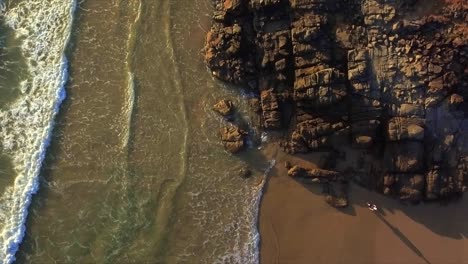 Aerial-drone-descending-shot-looking-straight-down-on-beach-and-rocks-with-a-woman-beachcomber