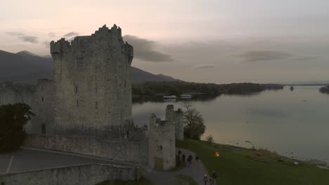 Aerial-uprising-shot-of-old-castle-at-a-lake-while-sunset-reflecting-on-water-surface