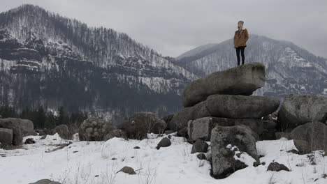 A-girl-stands-on-boulders-with-snowy-mountains-around-her