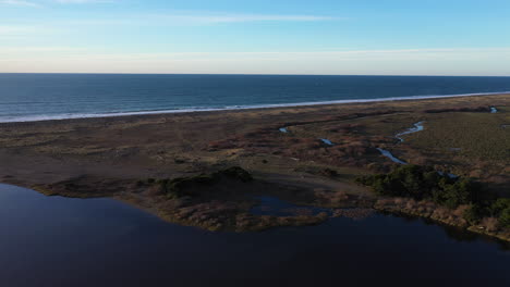 Drone-flying-over-the-edge-of-Floras-Lake,-showing-the-Pacific-Ocean-divided-by-a-strip-of-land,-as-well-as-the-start-of-New-River