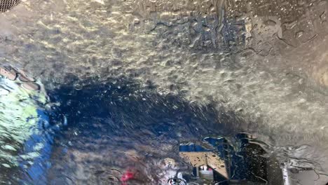 Car-going-through-an-express-car-wash-with-water-pouring-down-and-splashing-off-soap-and-grime-on-the-front-dash-window