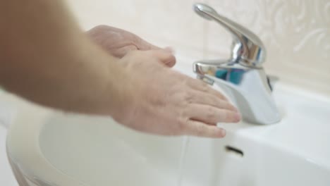 Man-washes-hands-in-bathroom-sink