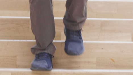 Close-up-of-a-male-walking-down-a-broad-wooden-modern-staircase-with-dark-shoes-and-jeans-on