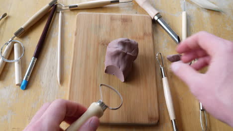 Close-up-on-the-hands-of-an-artist-or-sculptor-cutting-and-carving-a-strangely-satisfying-soft-brown-modeling-clay-sculpture-with-a-tool