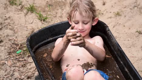 young-boy-playing-in-mud-in-wheelbarrow-filled-with-water