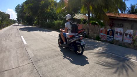 A-following-shot-of-a-man-riding-a-motorcycle-in-the-rural-streets-of-the-island-of-Bohol,-Philippines